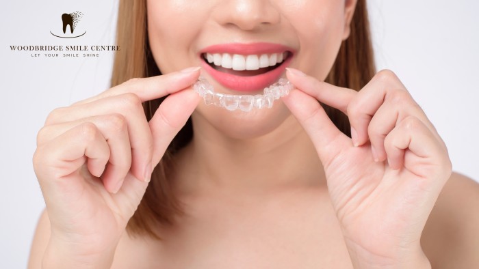 Young woman using both hands to fit an Invisalign aligner into her mouth