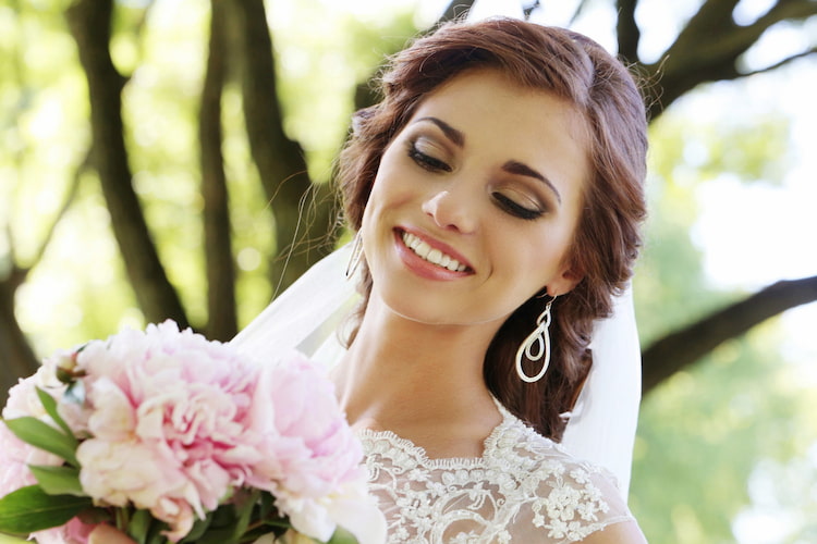 Bride in wedding dress smiling with bouquet outdoors.