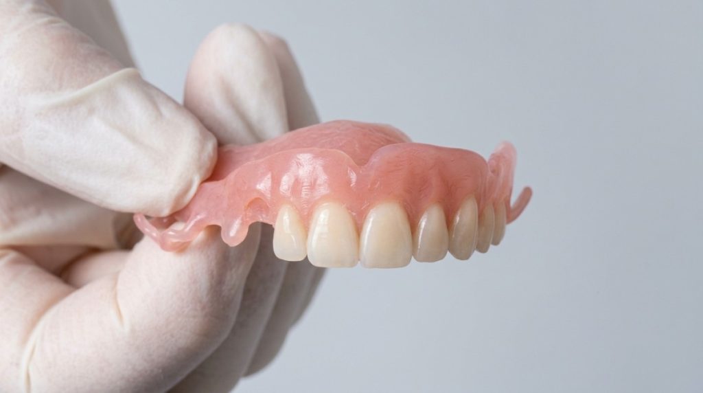 A close-up of a flexible partial denture for upper teeth being held in one hand.