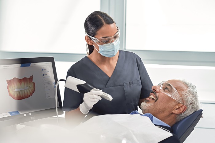 A dentist examining a patient and performing a digital scan to assess their suitability for flexible partial dentures for upper teeth.