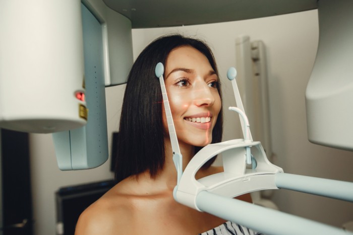 A woman at a dental clinic having her head positioned inside a scanning device to capture 3D scans of her teeth and jaw for Digital Smile Design.