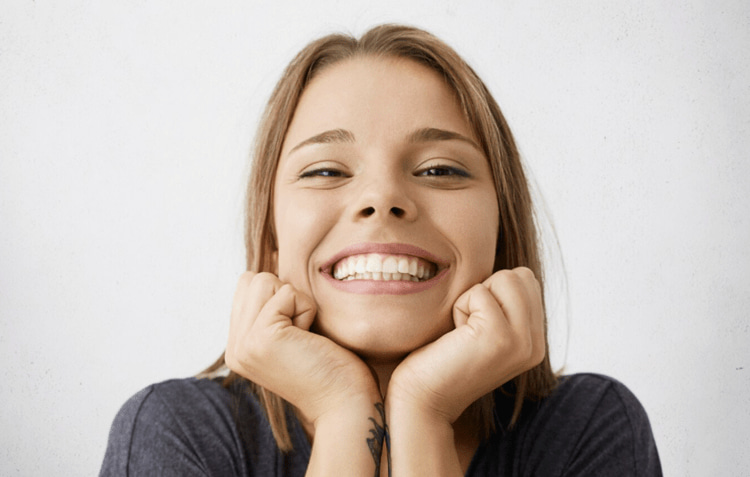 Woman smiling with hands on cheeks showing white teeth.