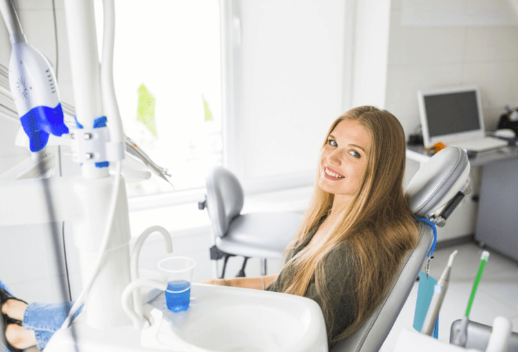 Smiling woman in dental chair with whitening light setup.