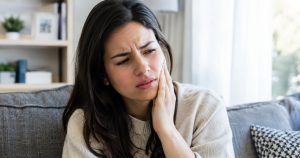 A worried woman sitting on a sofa at home, thinking "dentist chipped my tooth during cleaning"