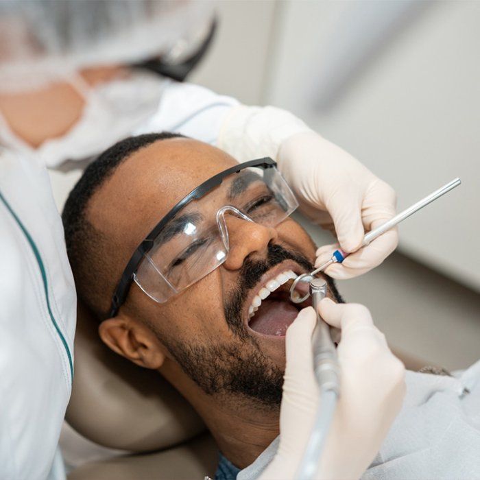 A young man receiving a regular dental cleaning to help prevent complications from heavy dental cleanings